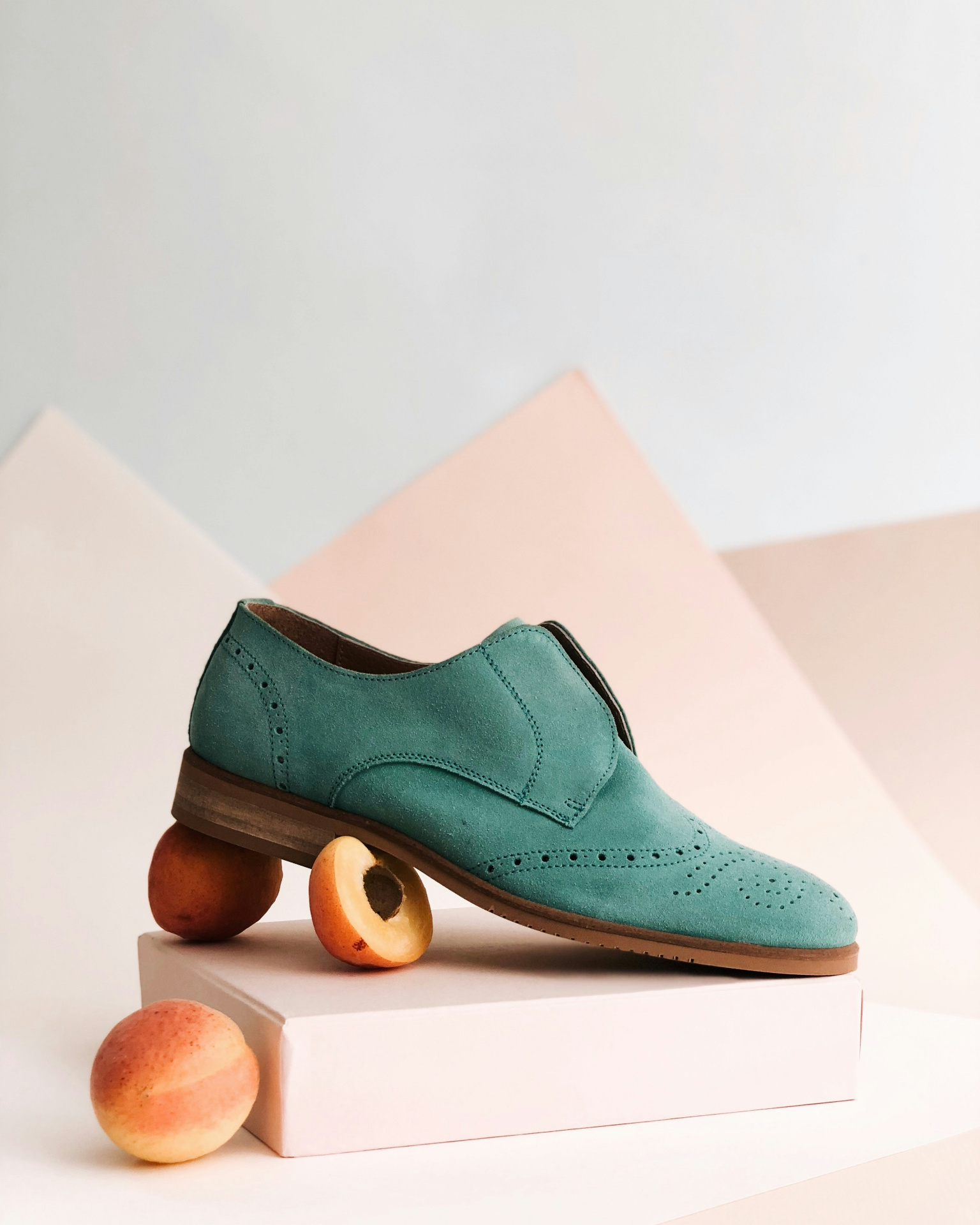 Teal suede dress shoe styled with fresh peaches on a minimal pastel set