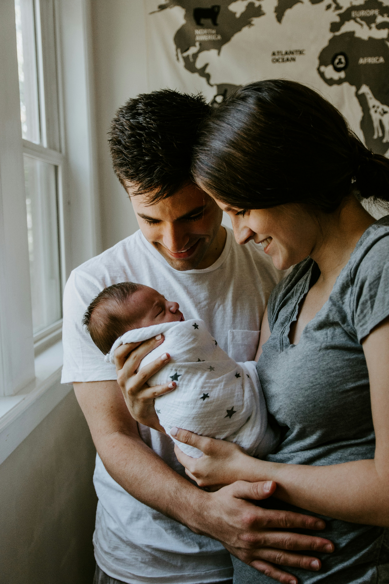 Loving parents holding their newborn baby wrapped in a star-patterned blanket by a sunlit window